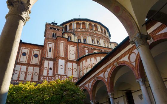 Blick in den Innenhof der Kirche Santa Maria delle Grazie in Mailand mit Renaissance-Arkaden und Kuppel im Sonnenlicht.