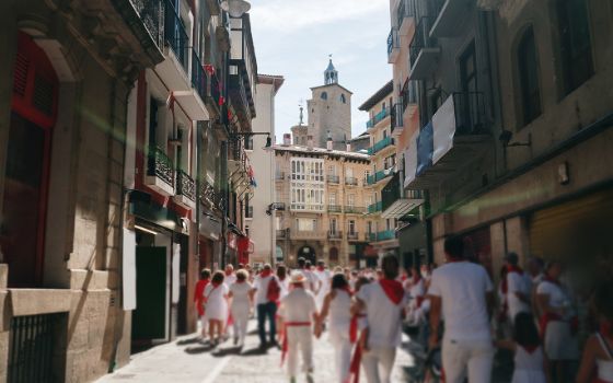 Viele Menschen mit weisser Kleidung gehen in einer schmalen Gasse, die Häuser sind teilweise verziert und haben kleine Balkone. 