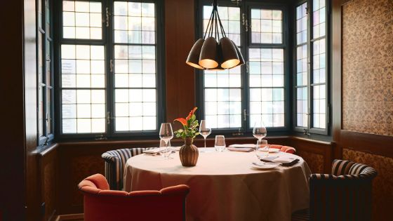 Eingedeckter runder Esstisch mit vier Polstersesseln an einer Fensterfront in einem Erker.