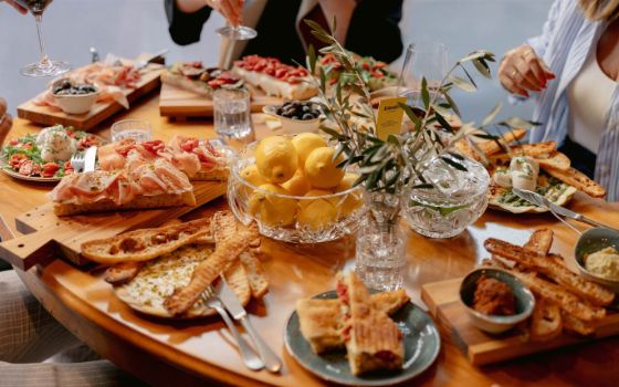 Italienische Antipasti auf gedecktem Holztisch mit Wein und mehreren Personen